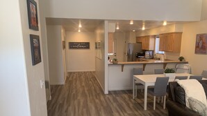 A modern kitchen with wooden cabinets, a stainless steel refrigerator, and a dining area with a white table and grey chairs.