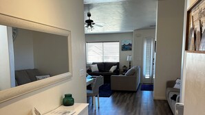 A modern, well-lit living room with a white console table, a dark sofa, and a window with blinds.