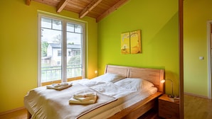 Une chambre à coucher avec un lit en bois, une table de chevet, une fenêtre avec des stores et un mur vert.