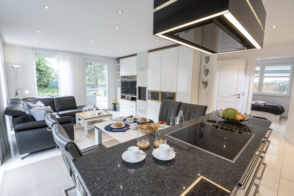 A modern kitchen with a central island, white cabinetry, and a dining area with a black table and chairs. - Vacation apartment Rudi's Huus, holiday apartment mediation North Sea - Rudi's Huus (Varel)