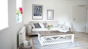 A modern living room with a white sofa, a wooden coffee table, and two framed artworks on the wall.
