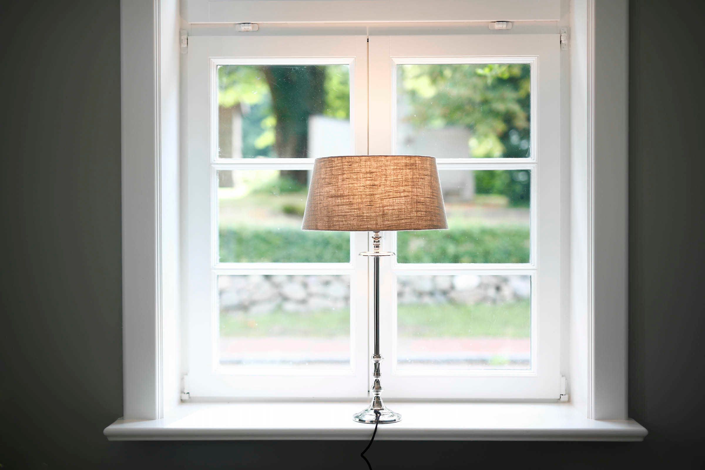 A floor lamp with a woven shade positioned in front of a white-framed window.