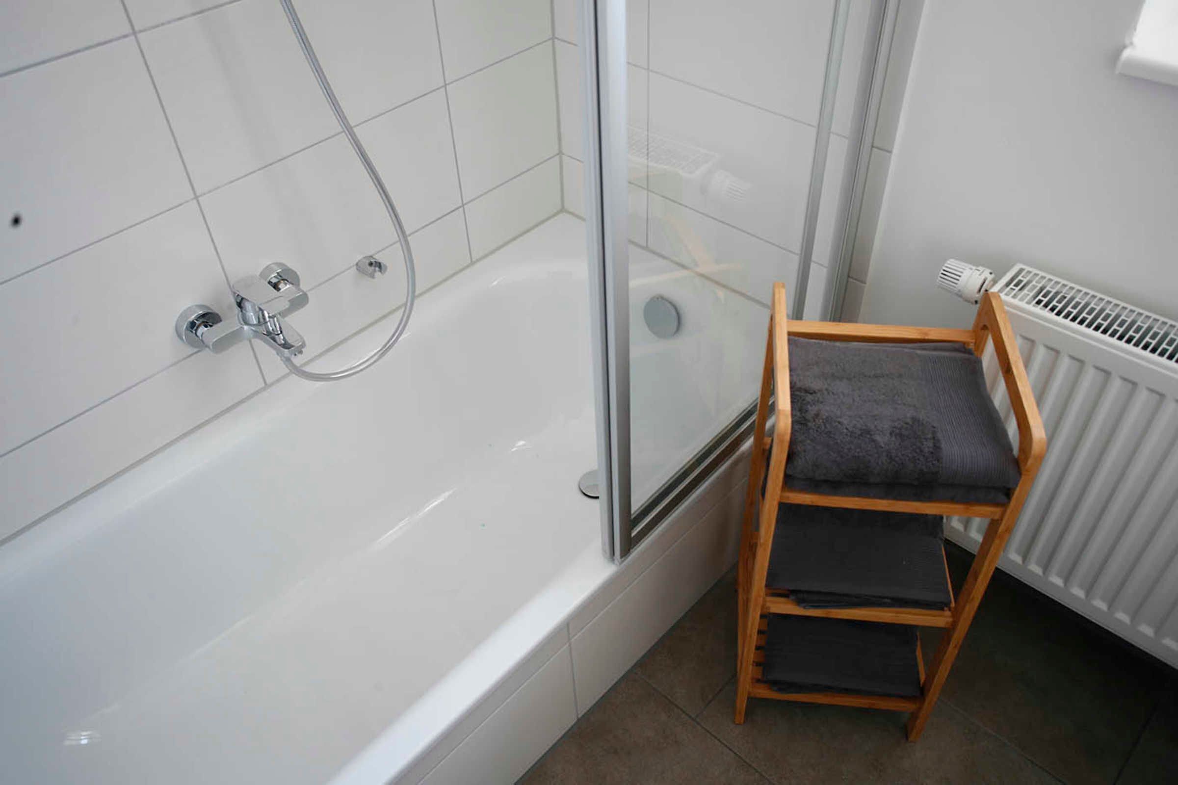 Un baño con una bañera blanca, una silla de madera con cojín y un radiador blanco.