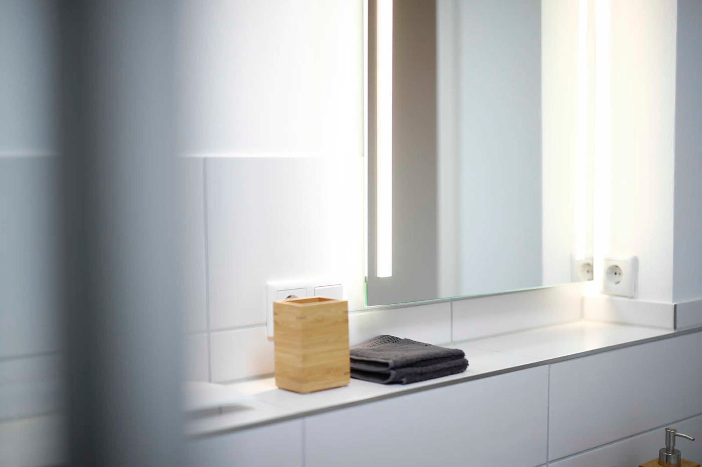 A modern bathroom with a glass partition, a wooden container, and a folded towel on the counter.