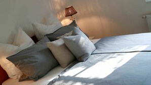 Ein ordentlich bezogenes Bett mit vielen Kissen, einer Nachttischlampe und einem Heizkörper an der Wand.