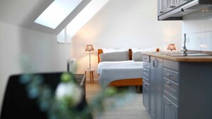Un dormitorio compacto con tragaluz, una mesita de noche con lámpara y cama con cabecero gris.