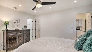 Een slaapkamer met een bed, een dressoir, een plafondventilator en een deur naar een andere kamer.