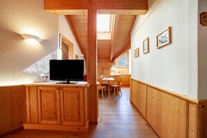 A wooden interior with a TV on a cabinet, a dining area, and framed pictures on the wall.