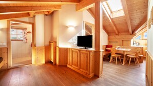 Un interior de madera con una televisión en un mueble, un comedor con sillas y un tragaluz.