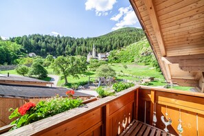 A wooden balcony with a view of a village, including a church and houses. - Holiday Apartment "Hof am Schloss Zirm" with Mountain View and Wi-Fi (Prad am Stilfserjoch)