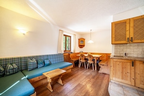 A cozy room with a blue sofa, wooden dining table, and chairs, a window with curtains, and wooden cabinets. - Holiday Apartment "Hof am Schloss Enzian" with Mountain View and Wi-Fi (Prad am Stilfserjoch)