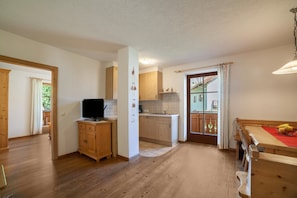 Eine geräumige Küche mit Holzausstattung, ein Essbereich mit Tisch und Bänken sowie ein Blick durch eine Glastür auf einen Außenbalkon.