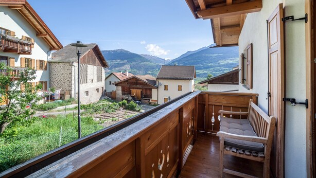 A balcony with a wooden bench, a view of a village, and a mountain range in the background. - Apartment "Hof am Schloss Edelweiss" with Mountain View and Wi-Fi (Prad am Stilfserjoch)