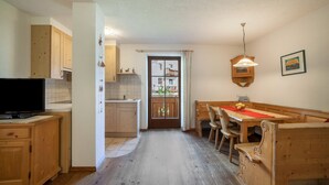 A kitchen with wooden cabinets, a dining table with chairs, a television, and a door with a glass panel. - Apartment "Hof am Schloss Edelweiss" with Mountain View and Wi-Fi (Prad am Stilfserjoch)