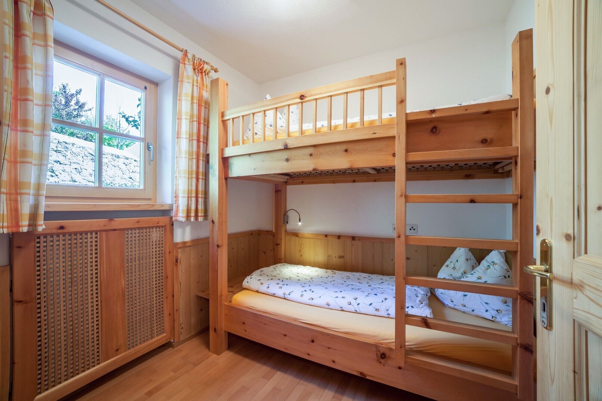 A bunk bed room with a window, wooden walls, and a radiator.