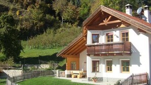 Un chalet a due piani con un balcone, un muro in pietra e una recinzione in legno.