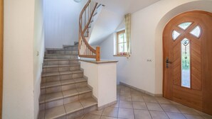 Una scala con ringhiere in legno che porta a un pianerottolo, una porta in legno con una finestra in vetro e una piccola finestra con tenda.