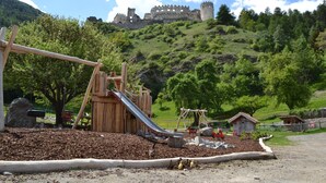 Un’area giochi con uno scivolo, altalene e un castello sullo sfondo.