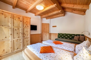A room with wooden ceilings, a bed with floral bedding, a green sofa with patterned cushions, and a television on the wall. - Vacation Home 'Ferienhaus Hof am Schloss' with Mountain View, Wi-Fi & Garden (Prad am Stilfserjoch)