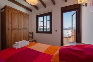 A bedroom with a bed, a wooden wardrobe, a window with a view, and a door leading to an outdoor area. - Holiday Home "Casa Teones" with Mountain Views, Private Pool and Terrace (Montecorto)