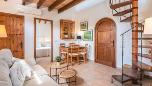 A cozy living room with a wooden staircase, a dining area with a wooden table and chairs, and a large wooden door. - Villa "Pau" with Mountain View, Pool, Wi-Fi & Terraces (Alcudia)