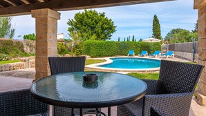 An outdoor patio with a round table and wicker chairs, a swimming pool, and lounge chairs in the background. - Villa "Pau" with Mountain View, Pool, Wi-Fi & Terraces (Alcudia)
