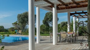 Ein überdachter Außenbereich mit Pool, Holzterrasse und weißen Säulen.