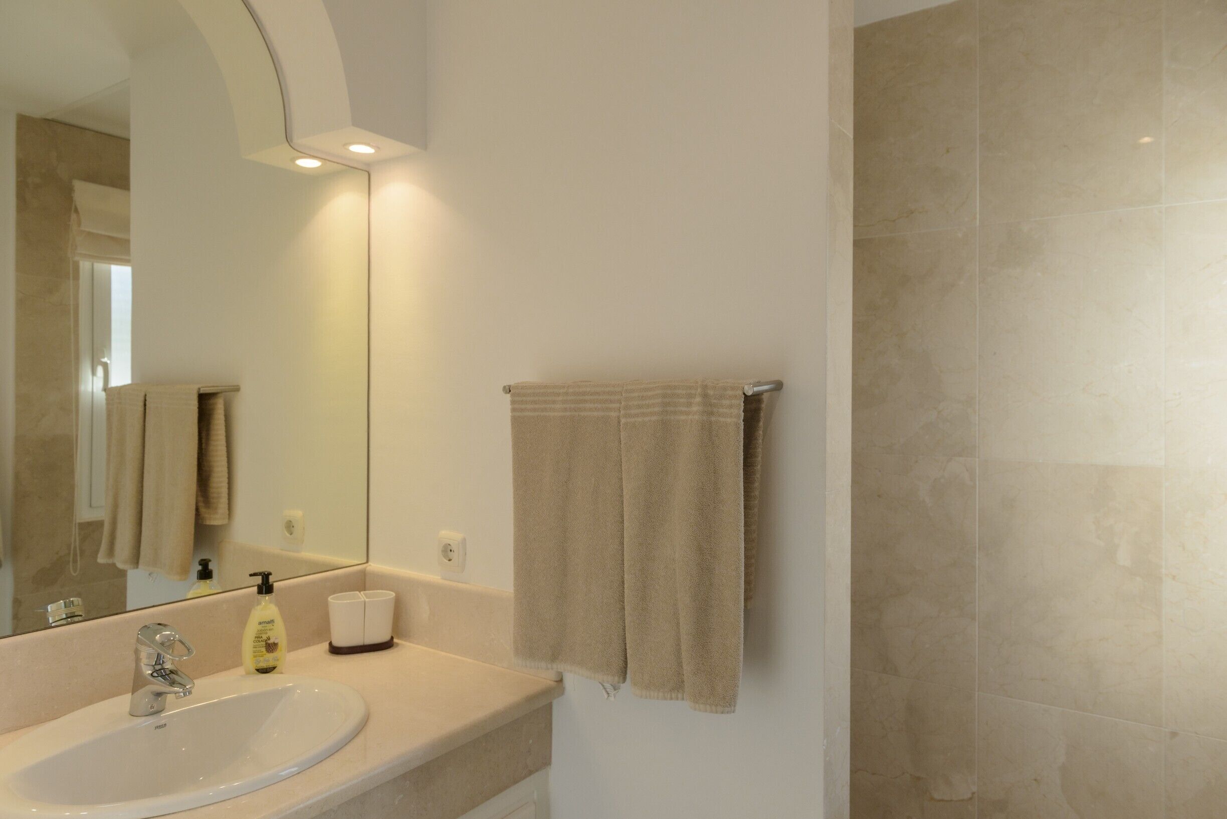 Baño con lavamanos, espejo, toallero y azulejos color crema.