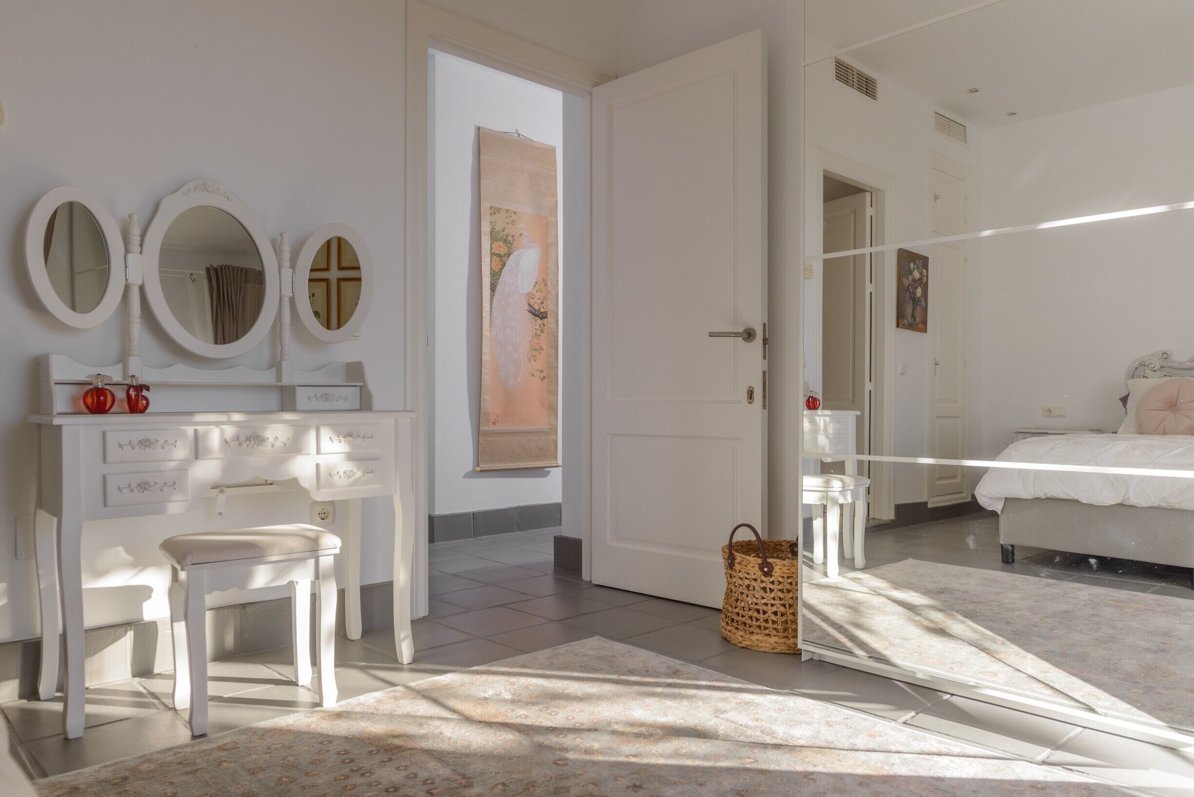 Une chambre à coucher avec un lit, une commode avec des miroirs, une chaise, une porte et un tableau au mur.