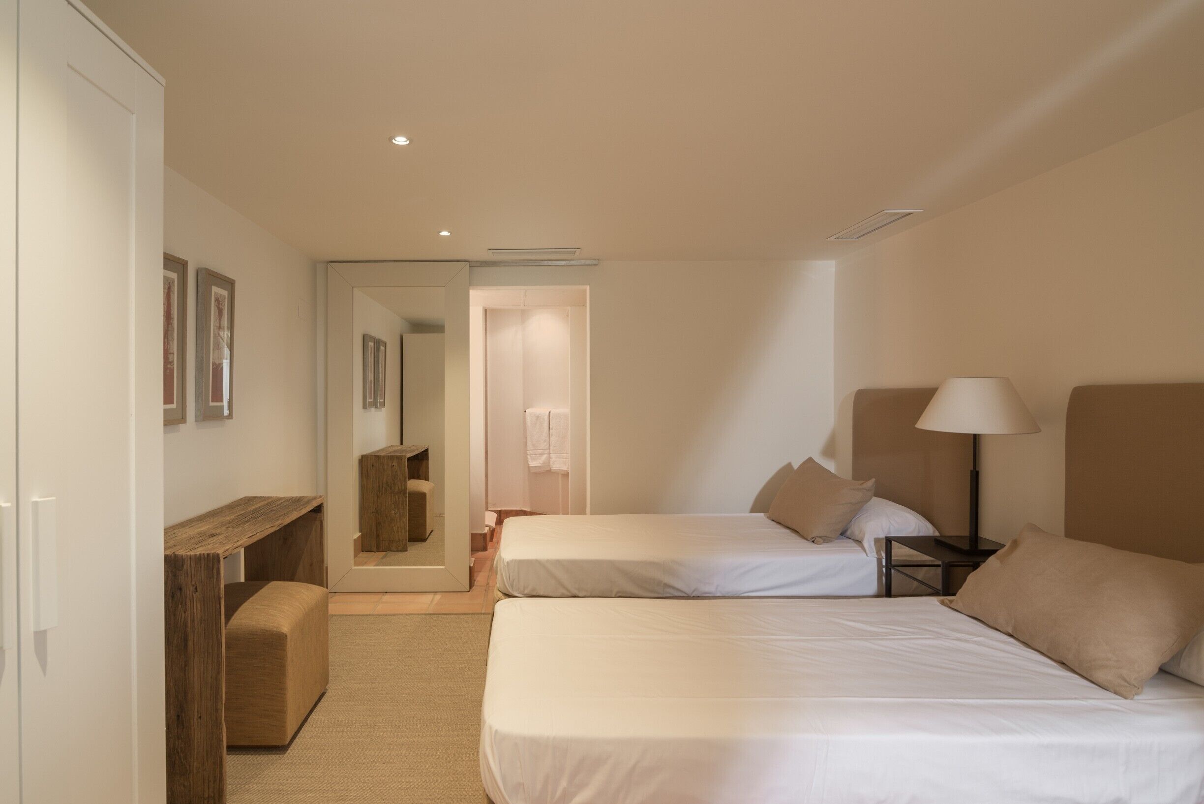 Una habitación de hotel con dos camas, un escritorio, un espejo y una mesita de noche con lámpara.