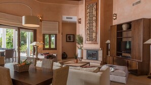 Amplia sala de estar con chimenea, televisor y comedor con mobiliario de mimbre.