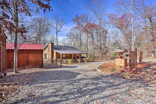 A rustic cabin with a red roof, a porch, and a gravel driveway.