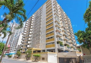 A multi-story residential building with balconies, a gated entrance, and a clear sky.
