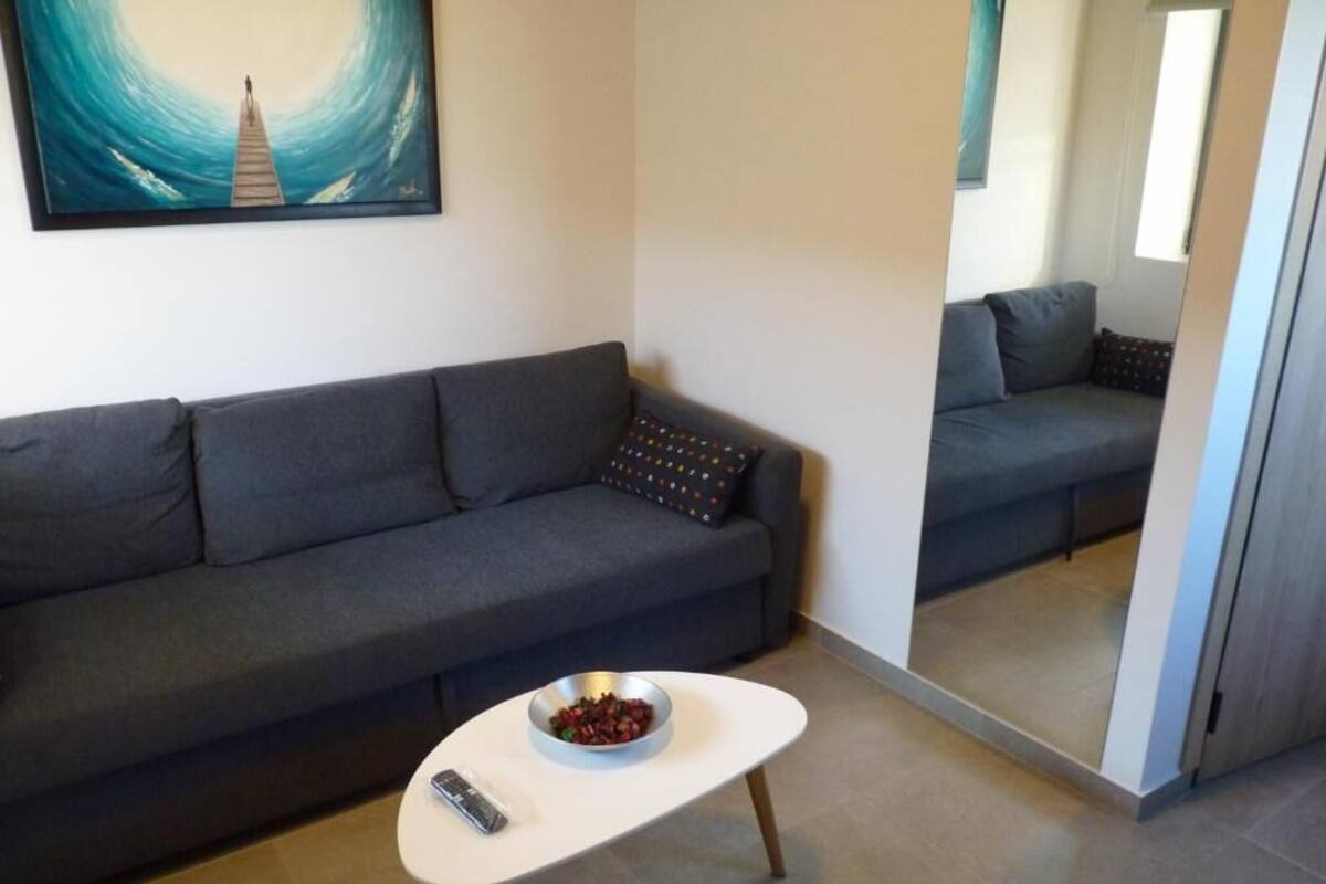 A modern living room with a grey sofa, a small white coffee table, and a bowl of fruit.