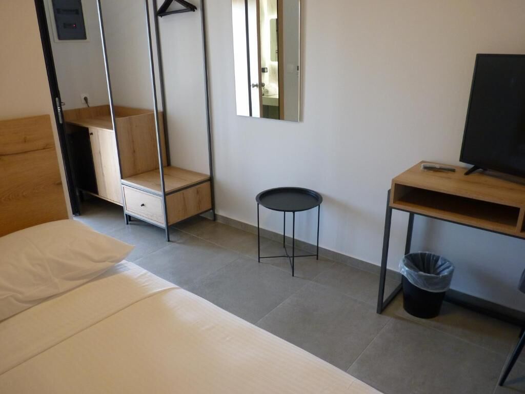 A room with a bed, a desk, a chair, a small stool, a trash bin, and a mirror.