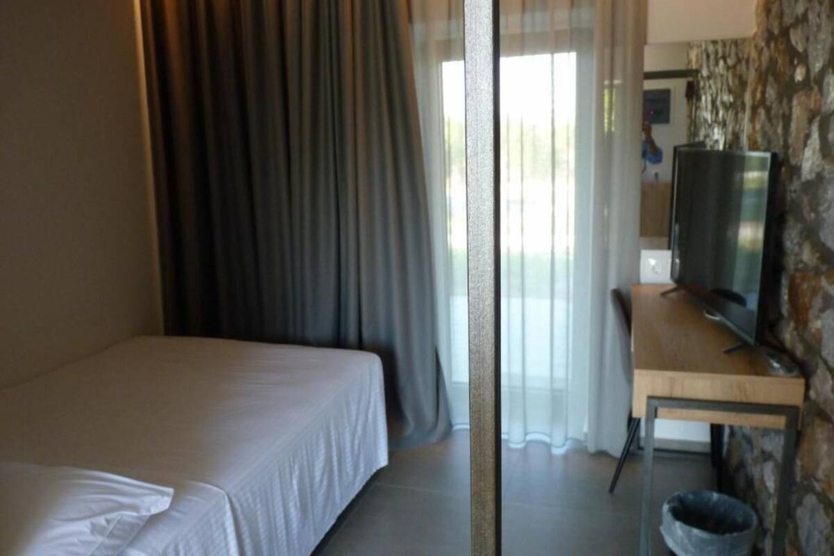 A hotel room with a bed, a desk with a television, and a stone wall.