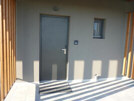 A closed door with a number plate, a small window, and a tiled floor with shadows.
