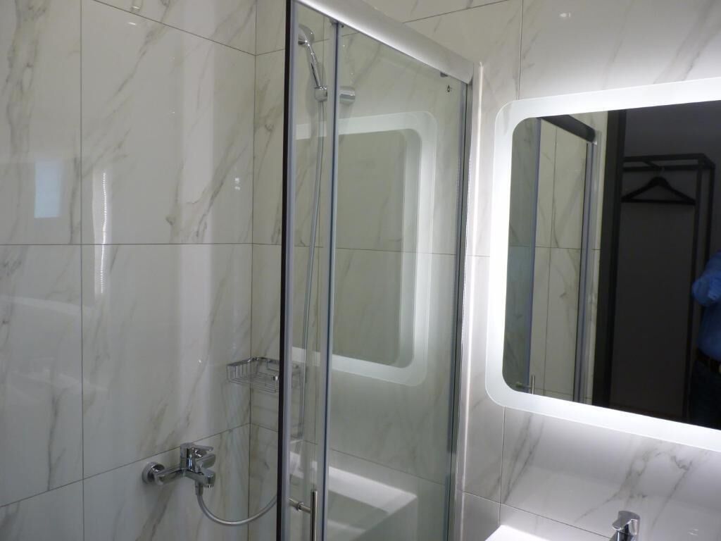 A modern bathroom with a glass shower enclosure, a white sink, and a large mirror.