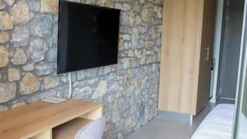 Una habitación con pared de piedra, televisor de pantalla plana sobre un escritorio de madera, una silla y un armario.