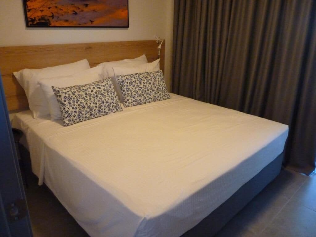 A neatly made bed with white linens and patterned pillows, a wooden headboard, and a painting on the wall.
