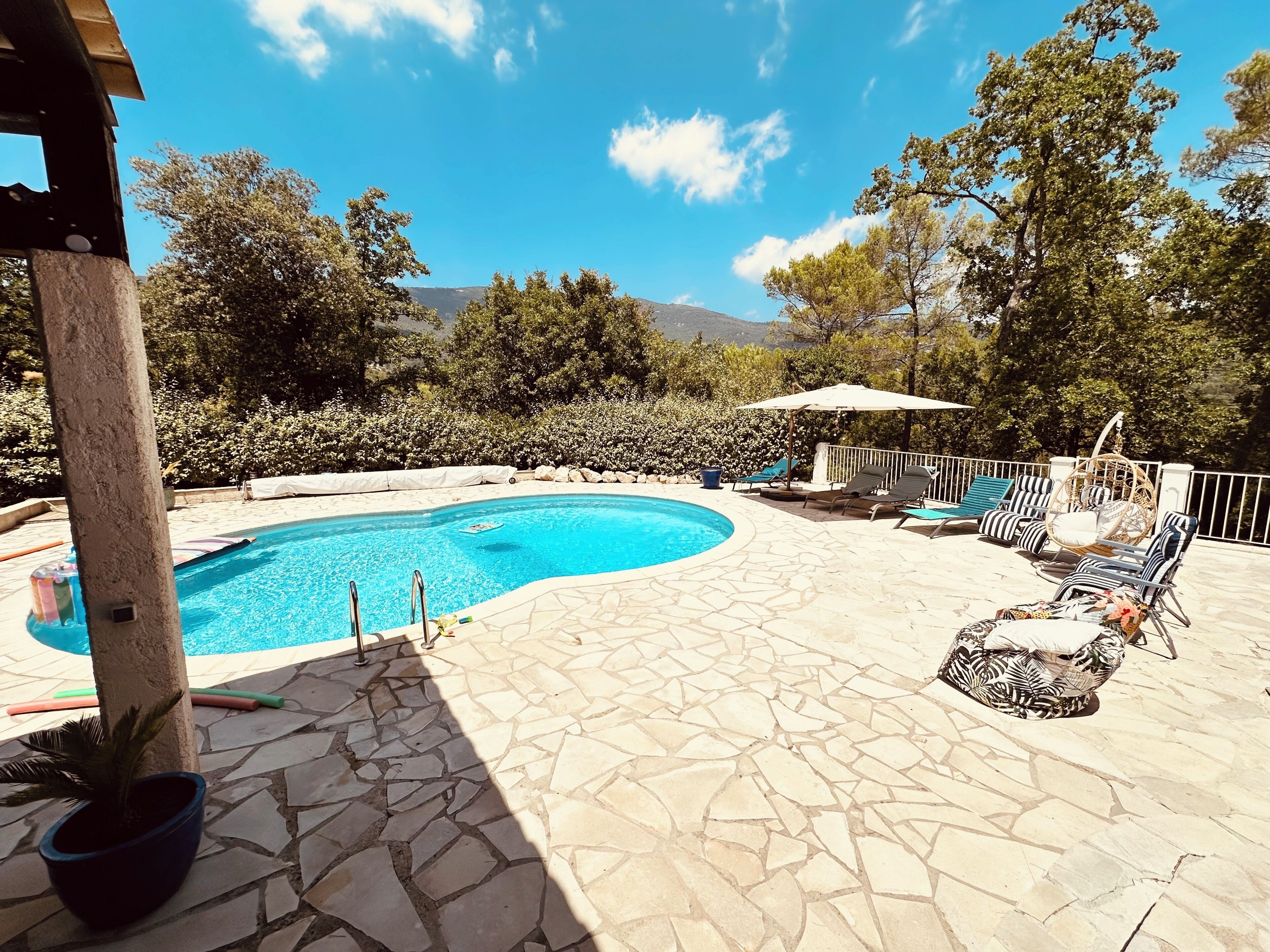 A swimming pool with stone tiles, lounge chairs, and a pergola.