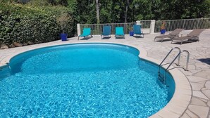 Une piscine aux eaux d’un bleu limpide, bordée de pierres, entourée de chaises longues et d’une rambarde en métal.