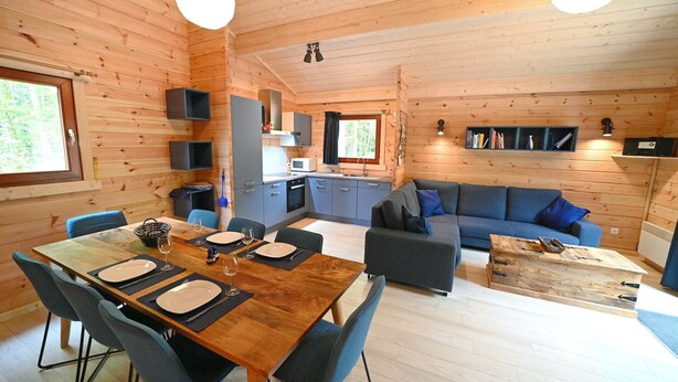 A wooden cabin interior with a dining area, kitchen, and living space.