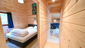 A wooden cabin room with a bed, a chair, and a painting on the wall.