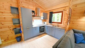 A compact kitchen with grey cabinets, a microwave, and a window with curtains.