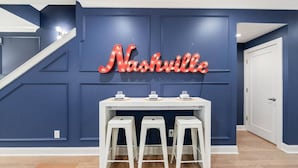 Una habitación con pared azul, una mesa blanca con tres taburetes y un letrero de neón que dice 'Nashville'.