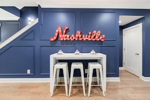 A room with a blue wall, a white table with three stools, and a neon sign spelling 'Nashville'.