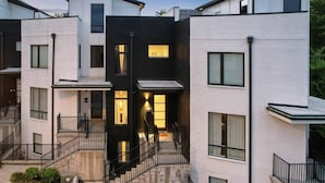 Un edificio residencial moderno de varios pisos, con balcones, una escalera central e ingreso bien iluminado.