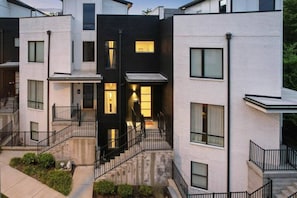 A modern multi-story residential building with balconies, a central staircase, and a well-lit entrance.