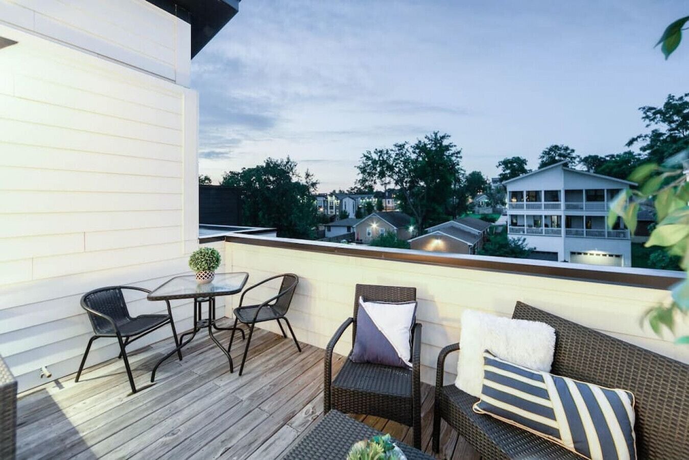 Un balcon extérieur doté d'une terrasse en bois, de meubles en osier et offrant une vue sur les bâtiments environnants.